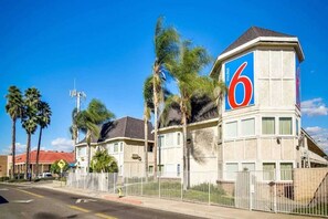 A motel with a prominent '6' sign, a fenced parking area, and palm trees.