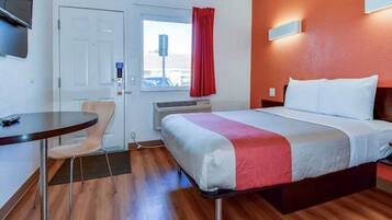 Habitación de hotel con cama, escritorio, silla, ventana con cortinas y un aire acondicionado de pared.