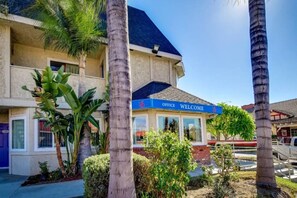 A hotel with a 'Welcome' sign, palm trees, and a clear blue sky. - 1 Queen Bed | Non-Smoking (Riverside)