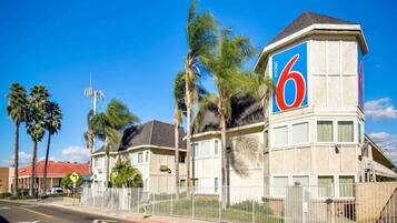 Un motel reconnaissable à son grand panneau avec le chiffre « 6 », un parking délimité par une clôture et des palmiers.