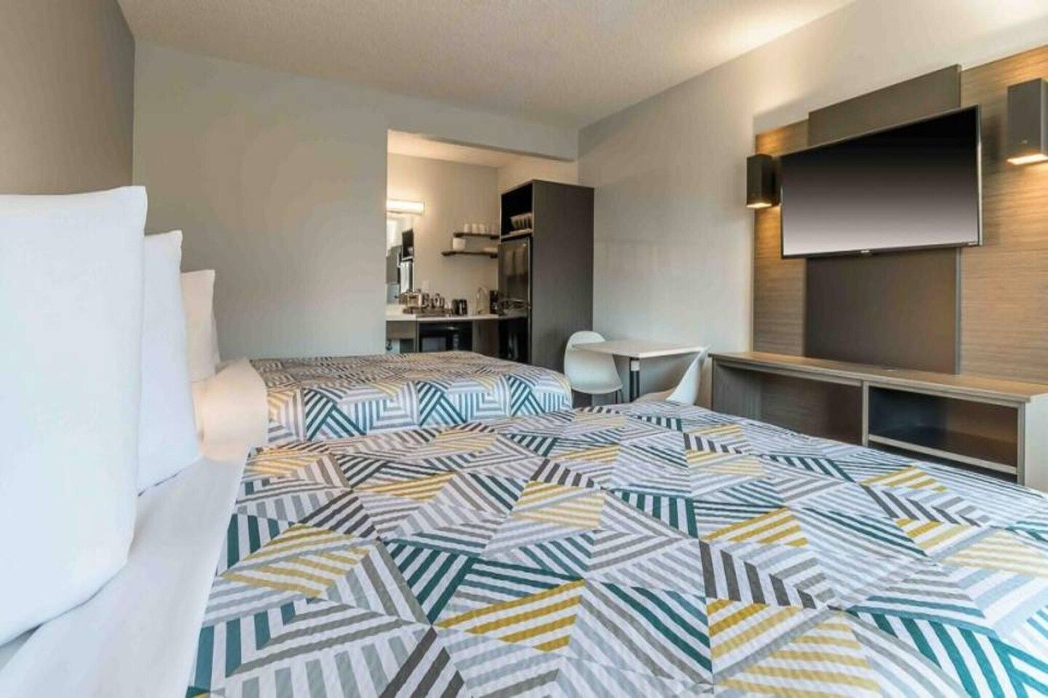 Ein Hotelzimmer mit einem Bett, einem Schreibtisch, einem Sessel und einem an der Wand befestigten Fernseher.