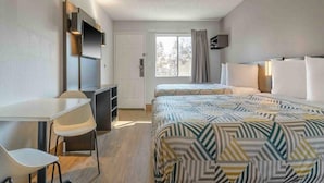 Une chambre d’hôtel avec un lit, un bureau, une chaise, une télévision et une fenêtre.