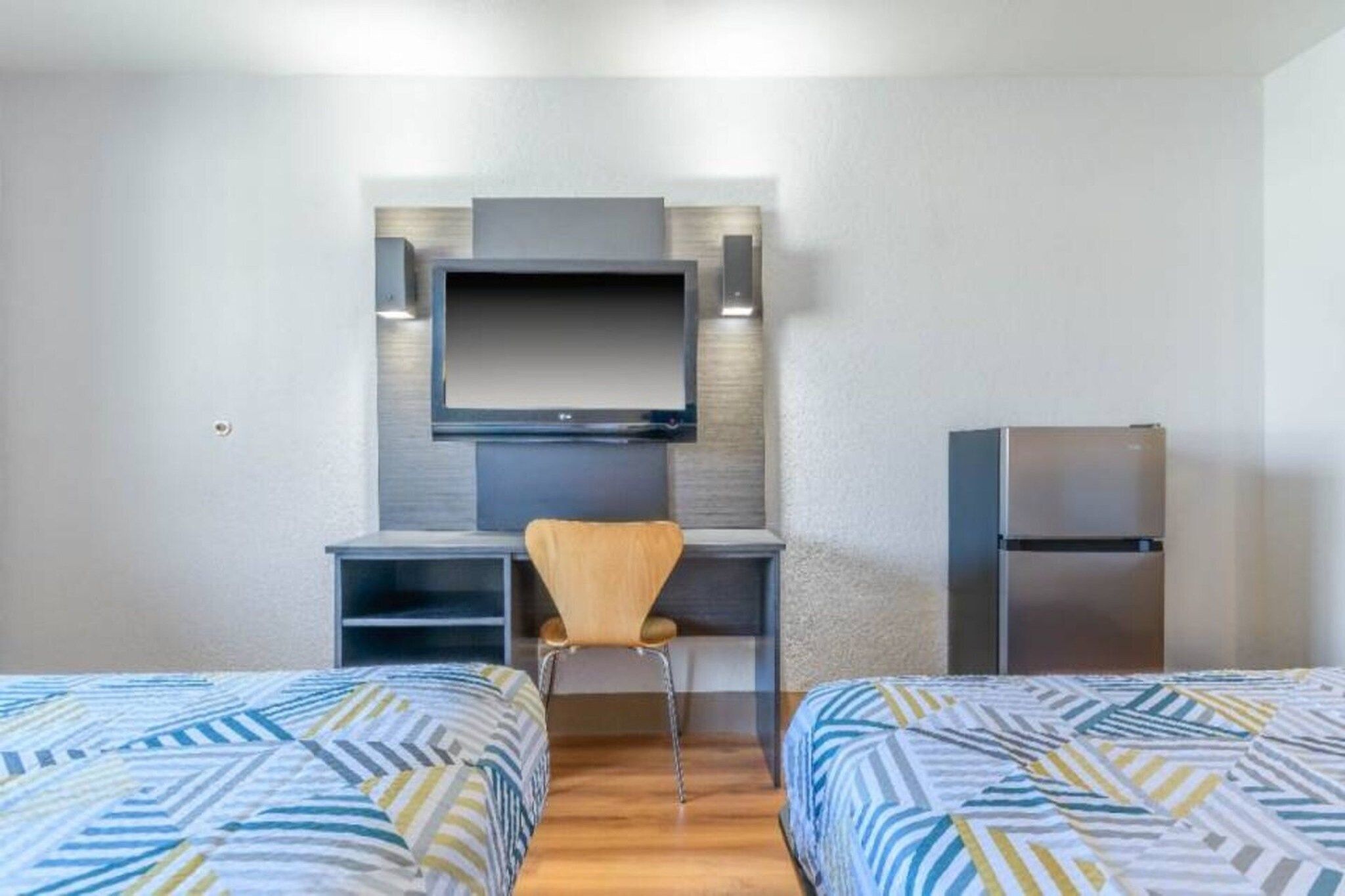 Ein Hotelzimmer mit zwei Betten, einem Schreibtisch, einem Stuhl, einem Fernseher und einem Kühlschrank.