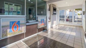 Un vestíbulo de hotel con una recepción, ventanas amplias y piso de baldosas.