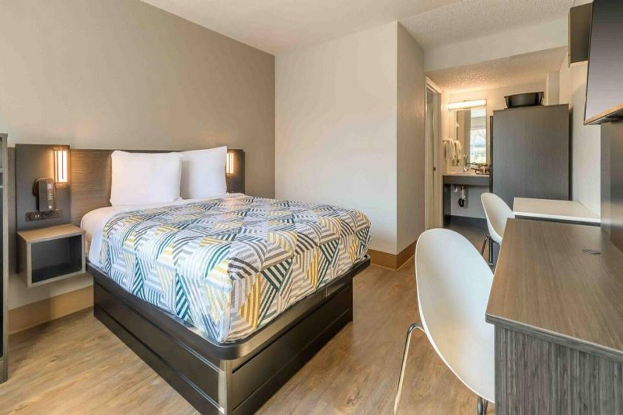 A modern hotel room with a bed, bedside tables, a desk, and a chair.