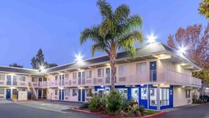 Un motel con varias habitaciones, estacionamiento y un área ajardinada con plantas.