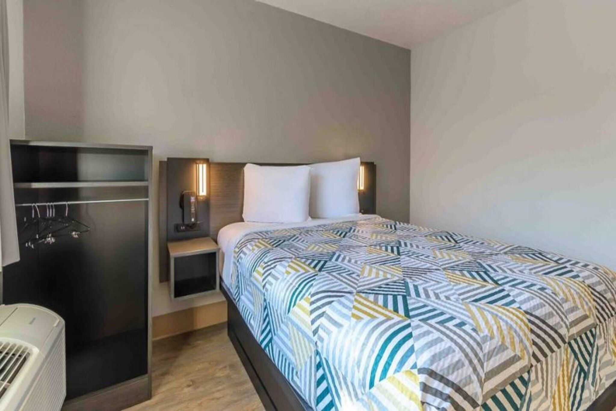 Ein Hotelzimmer mit Bett, Kleiderschrank, Nachttisch und Wandheizung.