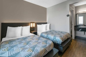 Quarto de hotel com duas camas, uma mesinha de cabeceira, um espelho e banheiro com pia e espelho.