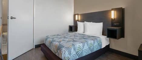 A modern hotel room with a large bed, a headboard with built-in lighting, and a wooden floor.