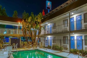 Um hotel com vários andares, piscina, área de estar externa e uma placa indicando o número 6.