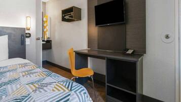 Een hotelkamer met een bed, een bureau, een stoel, een televisie en een wandlamp.