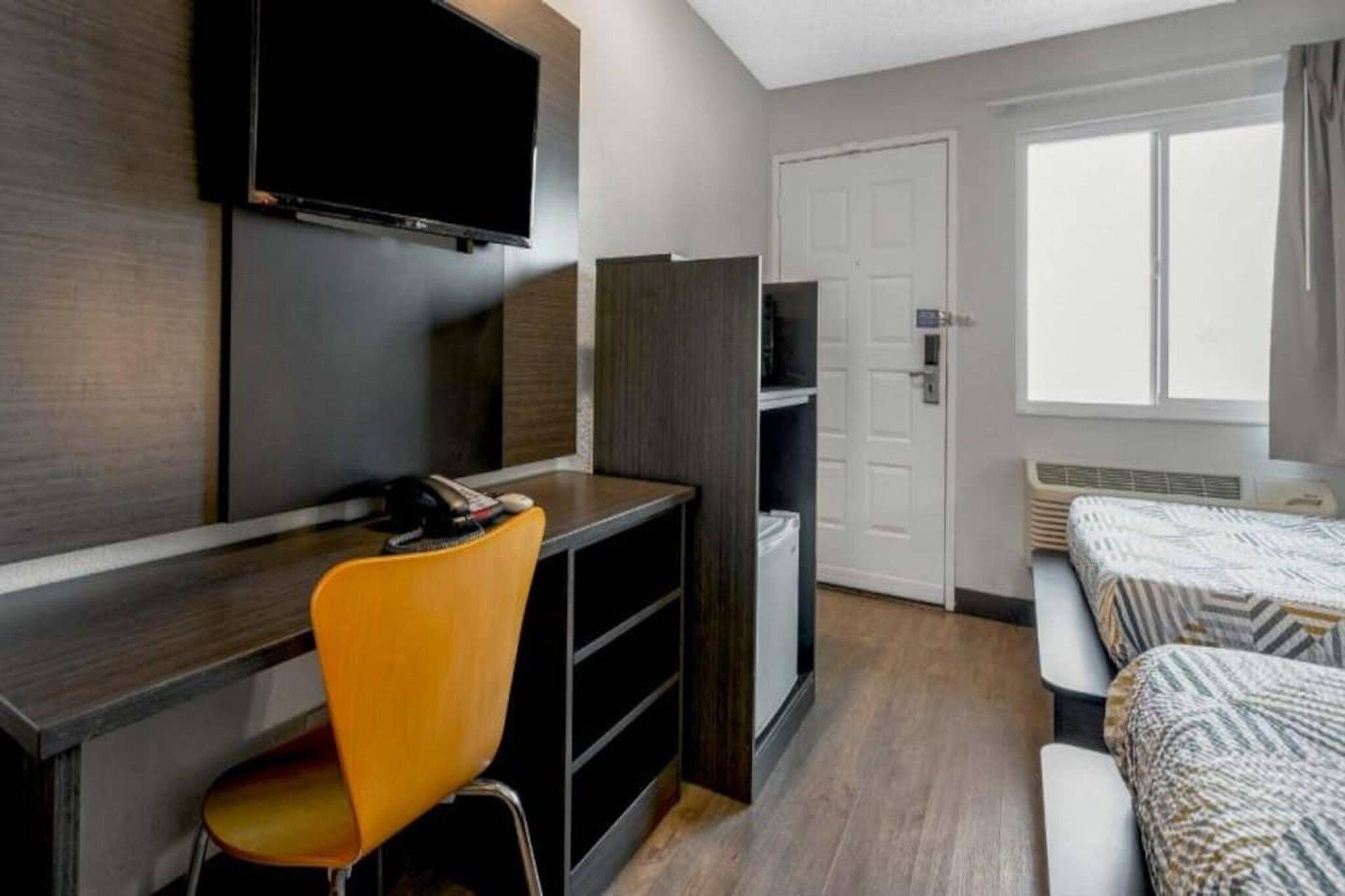 A hotel room with a desk, chair, television, wardrobe, and a bed with patterned bedding.