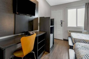 Habitación de hotel con escritorio, silla, televisor, armario y cama con ropa de cama estampada.