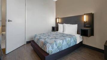 A modern hotel room with a large bed, a bedside table, a nightstand, and a wall-mounted light fixture.