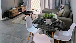 Uma sala de estar moderna com sofá, mesa de jantar com cadeiras, televisão na parede e janela com cortinas.