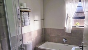 Casa de banho com cabine de chuveiro em vidro, sanita, banheira e lavatório.