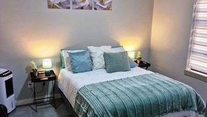 Quarto com cama, mesas de cabeceira, aquecedor e janela com persianas.