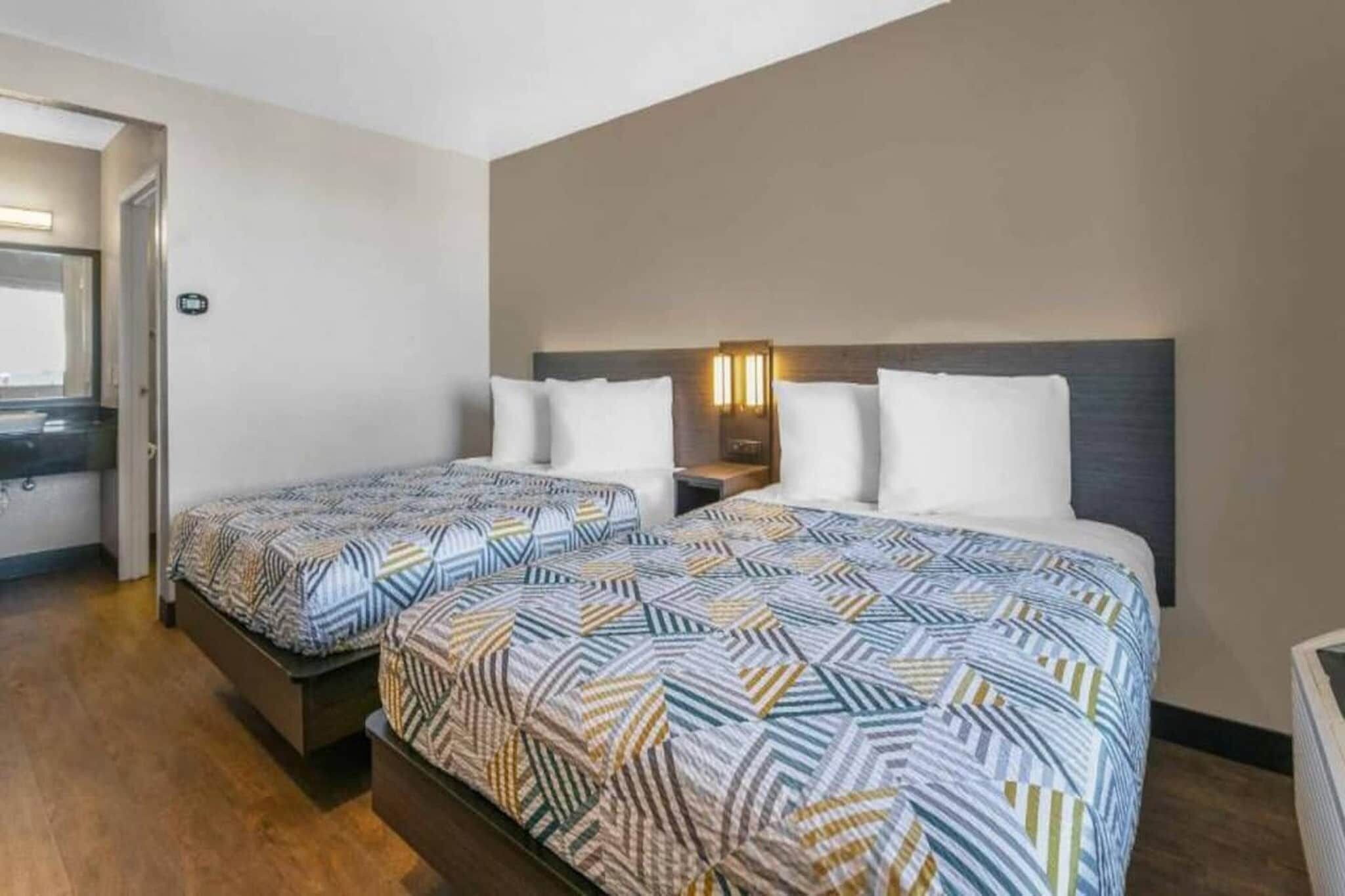 A hotel room with two beds, a nightstand, and a wall-mounted light fixture.