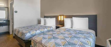 A hotel room with two beds, a nightstand, and a wall-mounted light fixture.