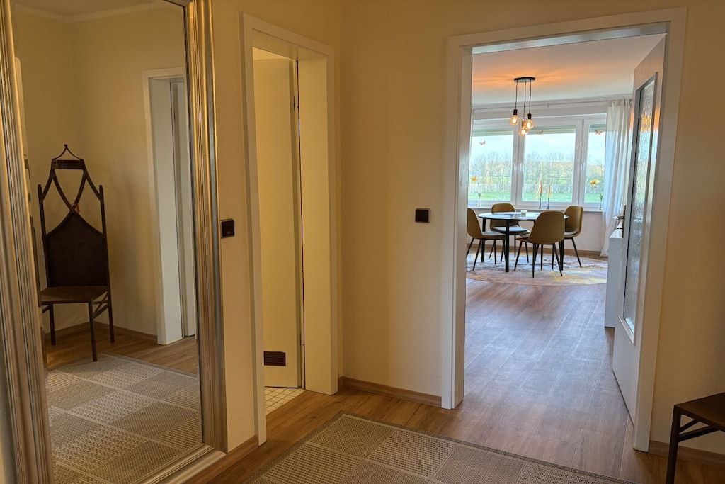 A hallway leading to a dining area with a table and chairs, a hanging chair, and a view through the door.