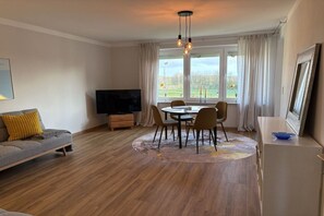 A living room with a sofa, a TV, a dining table with chairs, and a window with curtains. - Near the sea & plenty of sunshine (Cuxhaven)