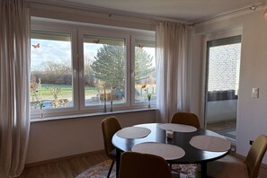 Un comedor con una mesa y sillas, ventanas amplias con cortinas, y vistas al exterior.