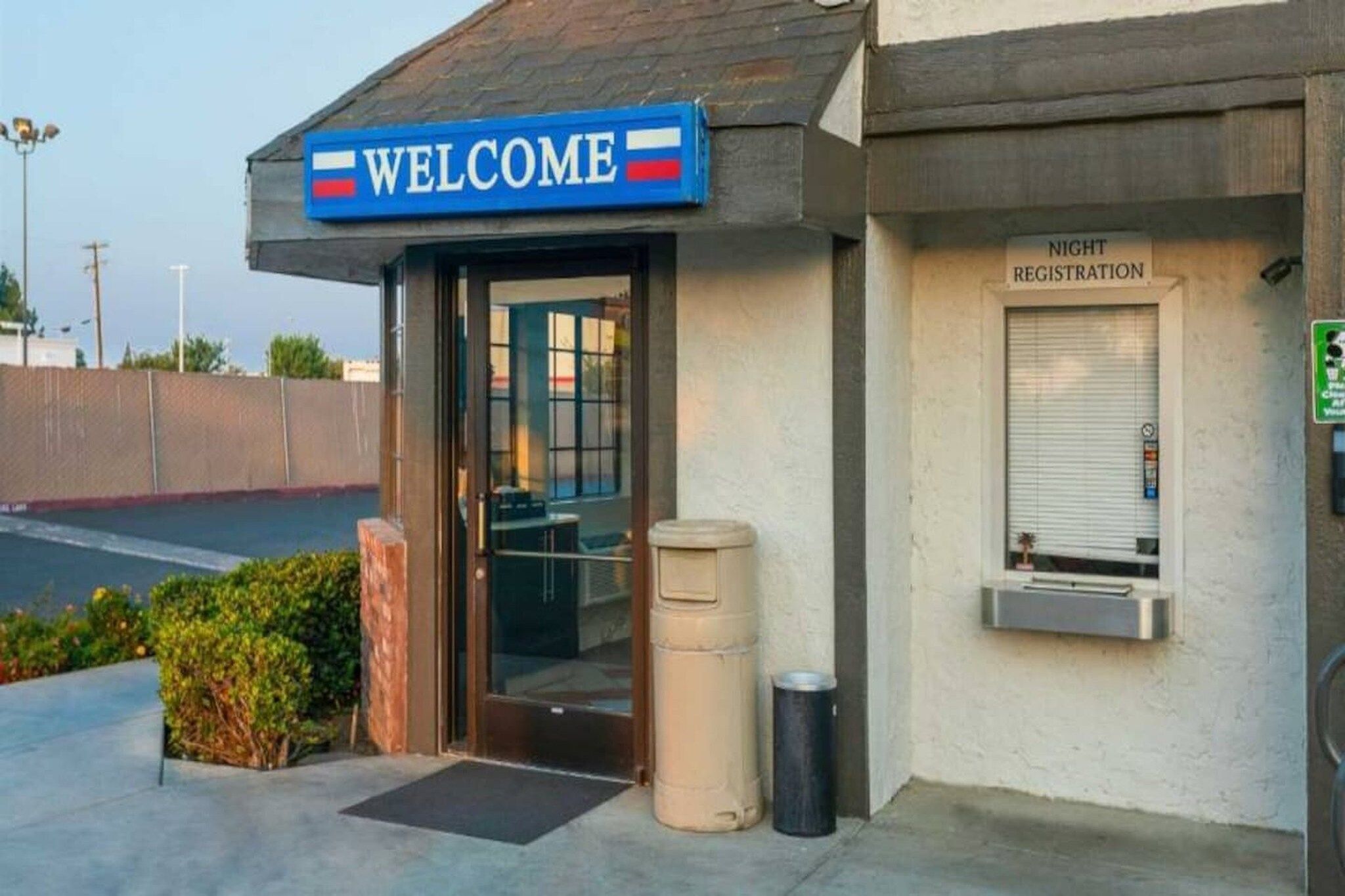 A building with a 'WELCOME' sign, a registration area, and a trash bin outside.