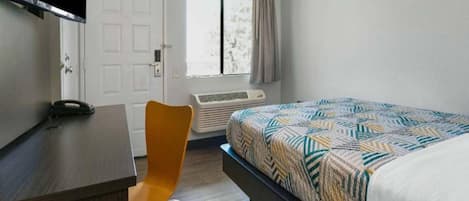 A bedroom with a bed, a desk, a chair, a TV, and a window.