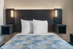 Habitació d'hotel amb un llit, dues taules de nit i làmpades penjades a la paret.