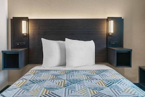 Quarto de hotel com cama, duas mesas de cabeceira e luminárias fixadas na parede.