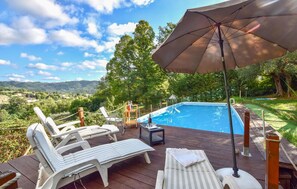 Eine Holzterrasse mit Liegestühlen und einem Pool mit Blick auf eine malerische Landschaft.