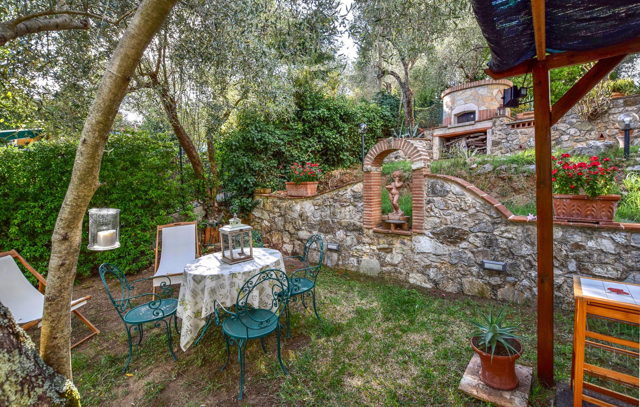 Un patio esterno con un muro in pietra, un piccolo forno a mattoni e una statua.