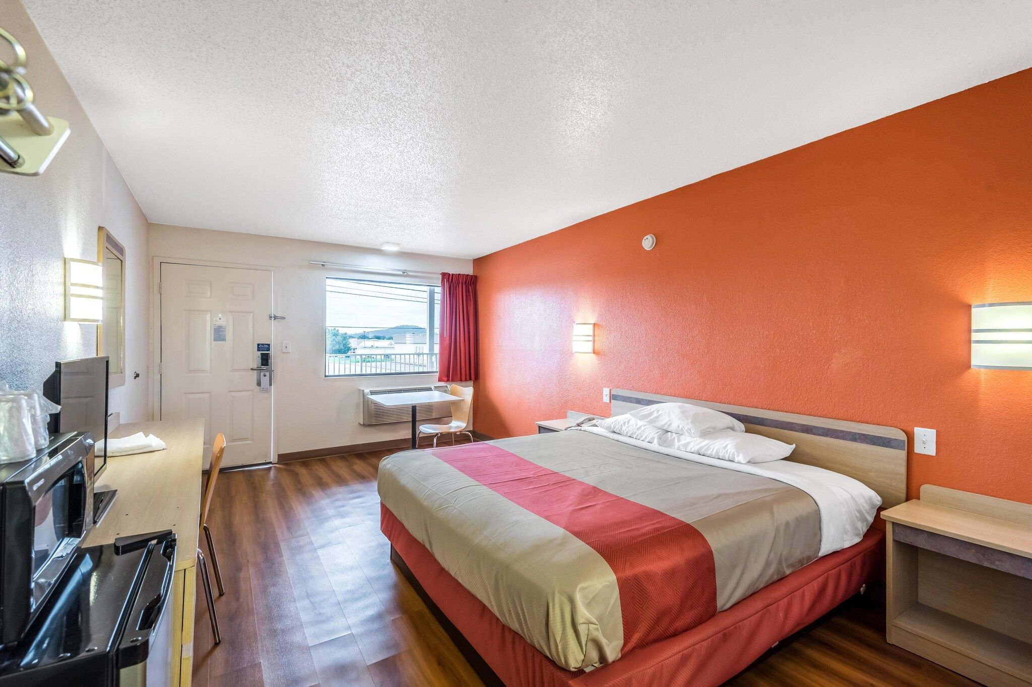 Une chambre d’hôtel avec un lit, un bureau, une chaise, une télévision et une fenêtre avec des rideaux.