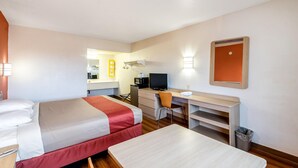 Habitación de hotel con cama, escritorio, silla y un pequeño cubo de basura.