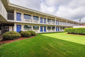 Een motel met een gebouw van twee verdiepingen, meerdere kamers met blauwe deuren en een verzorgd gazon.