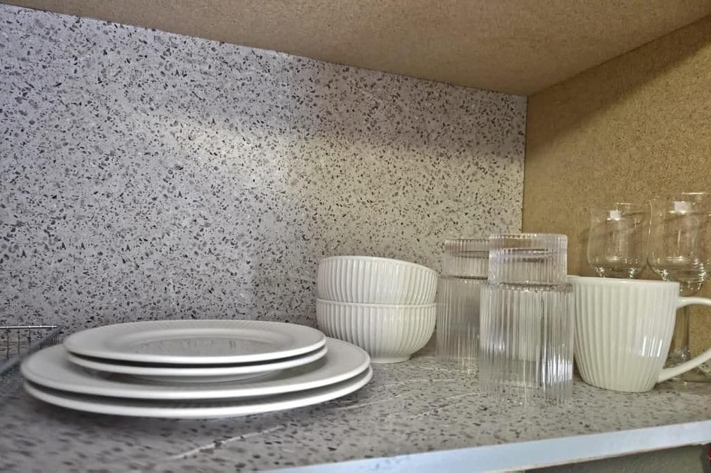 A kitchen counter with stacked plates, a white ribbed bowl, and clear glass mugs.