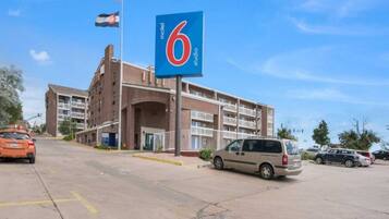 A motel with a large '6' sign, multiple floors, and a parking lot with cars.