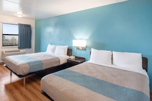 Une chambre d’hôtel avec deux lits, une fenêtre avec des rideaux, une table de chevet avec une lampe et un climatiseur fixé au mur.