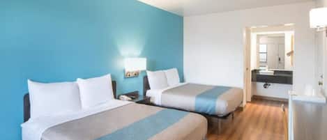 Une chambre d’hôtel avec deux lits, un bureau et une salle de bain visible à travers une porte ouverte.