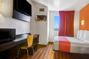A hotel room with a bed, a desk with a chair, a television, and a window with curtains.