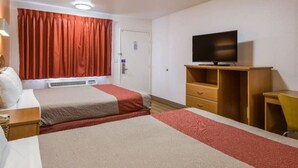Quarto de hotel com duas camas, televisão, escrivaninha e uma cadeira.