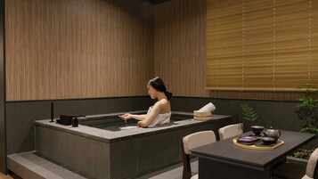 Un cuarto de spa con un jacuzzi, una mesa con juego de té y una ventana con persianas.