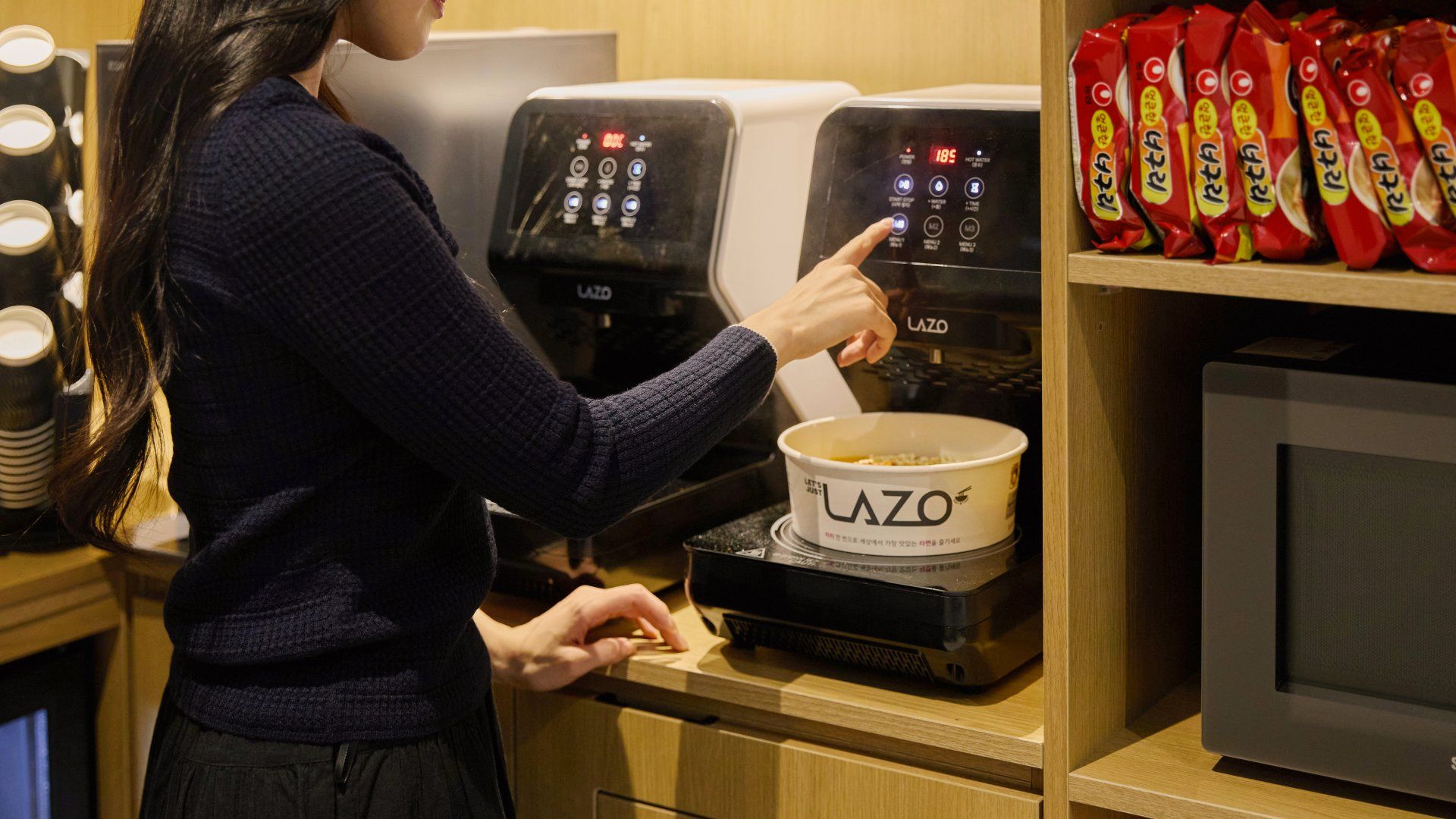 Iemand bedient een koffieapparaat met een bedieningspaneel waarop het merk 'LAZO' staat.