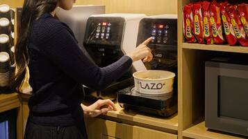 Iemand bedient een koffieapparaat met een bedieningspaneel waarop het merk 'LAZO' staat.
