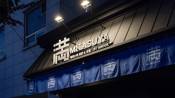 Fachada de edificio con letreros iluminados que muestran 'MITSASUYA' y un toldo azul con la misma marca.