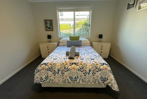 A bedroom with a bed, two bedside tables, a window, and a wall-mounted picture.