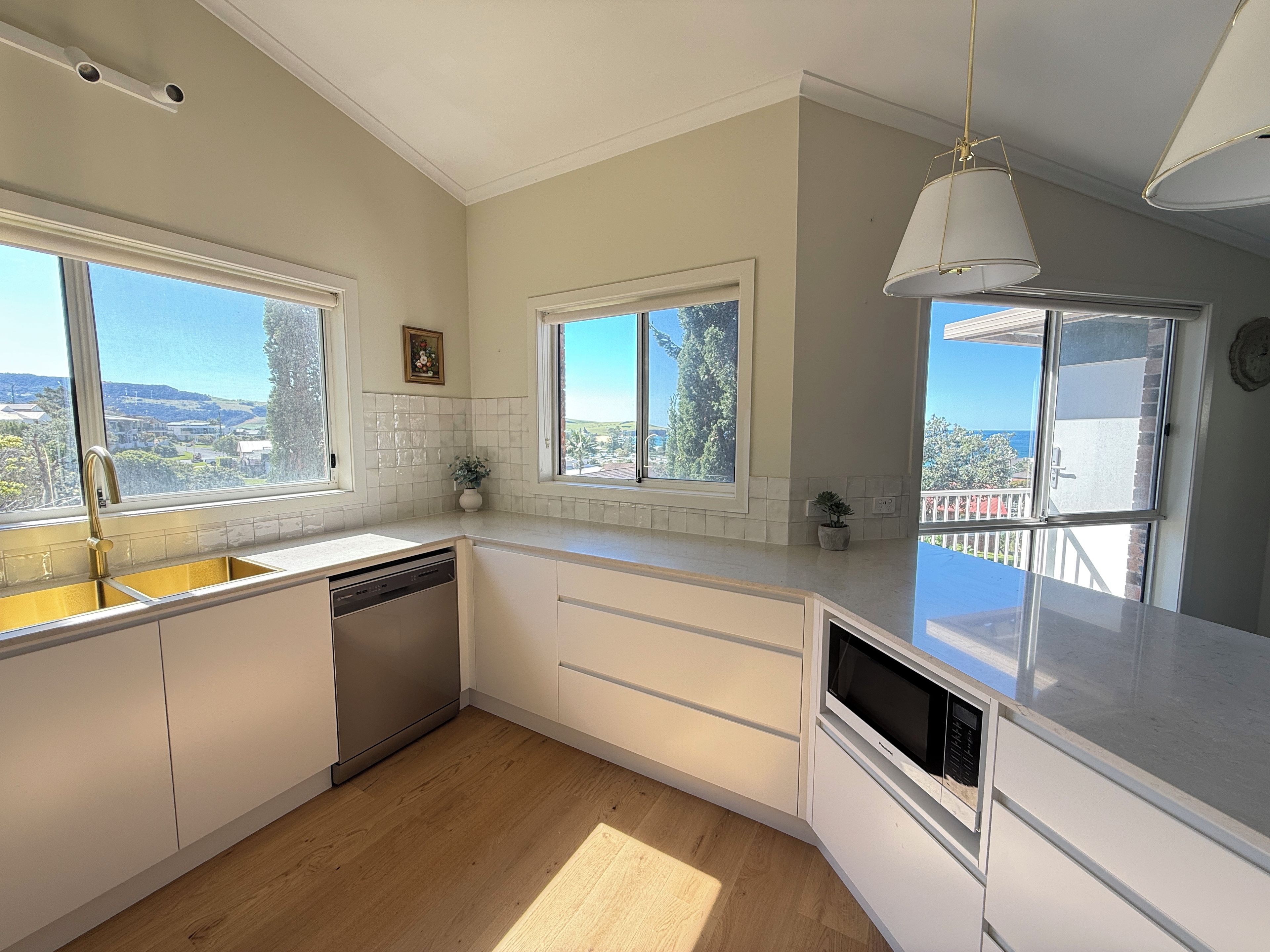 A kitchen with white cabinets, a dishwasher, and a view of the outdoors through large windows.