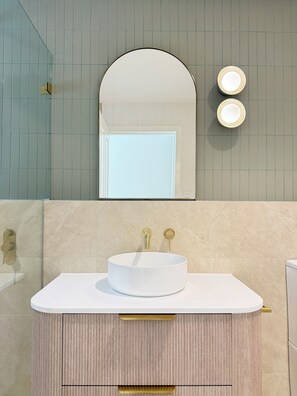 A bathroom with a round white sink, gold faucets, and a mirror above.