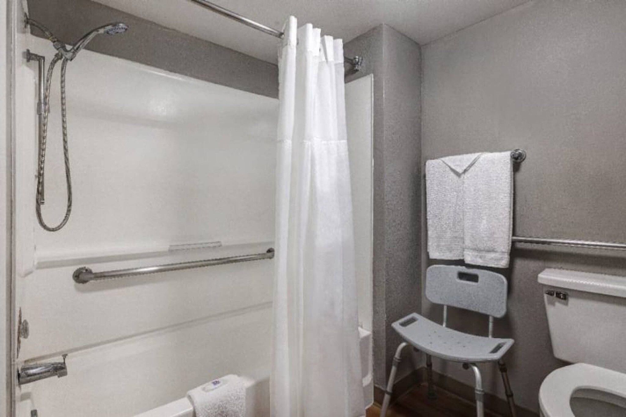A bathroom with a shower, a toilet, and a grab bar.