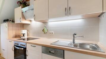 A modern kitchen with white cabinetry, a built-in oven, a coffee machine, and a stainless steel sink.